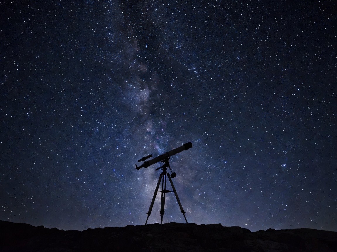 A lone telescope silhouetted against a star-filled night sky